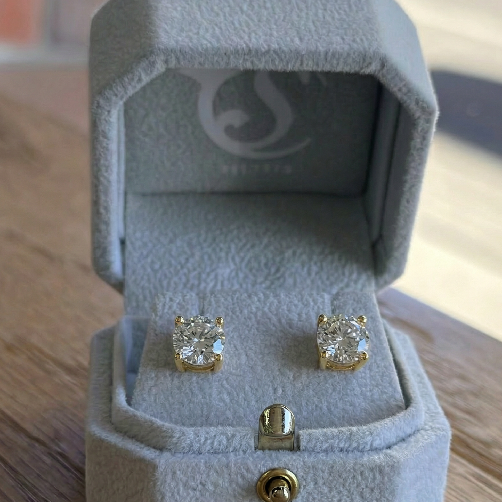 Diamond stud earrings in a light blue jewelry box on a wooden surface